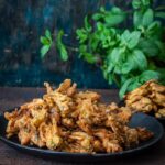 Crispy Onion Pakoda served on a black plate along with baked pakodas.