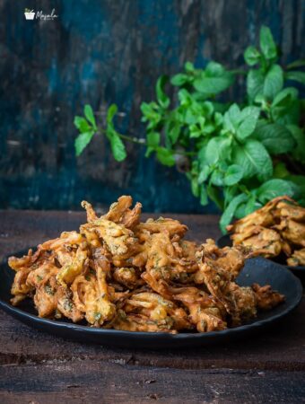 Crispy Onion Pakoda served on a black plate along with baked pakodas.