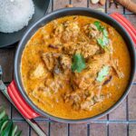 Chicken korma served in a red bowl with rice on the side.