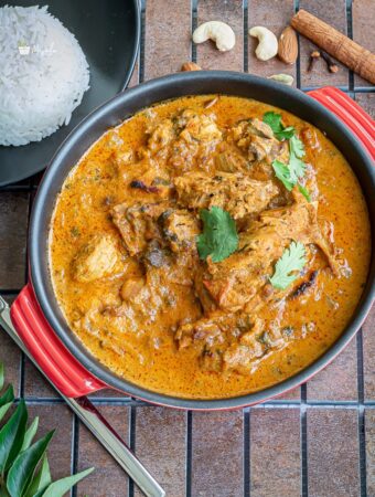 Chicken korma served in a red bowl with rice on the side.