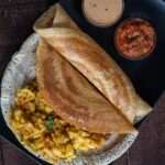 Barnyard Millet Dosa served on a bleck plate with potato masala and two chutneys.