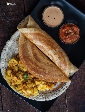 Barnyard Millet Dosa served on a bleck plate with potato masala and two chutneys.