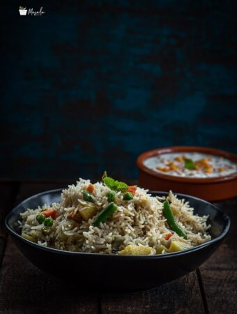 Vegetable Biryani served in a black bowl with Boondi Raita on the side.