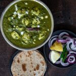 Palak paneer curry served with roti and onions one the side.