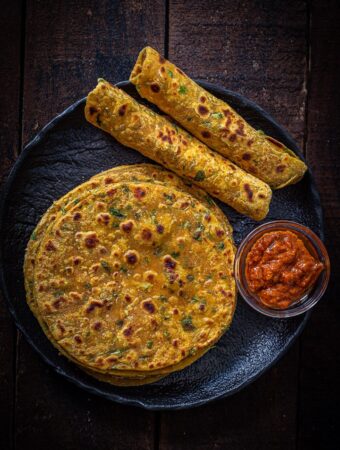 Gujarati Methi Thepla served on a black plate with mango pickle